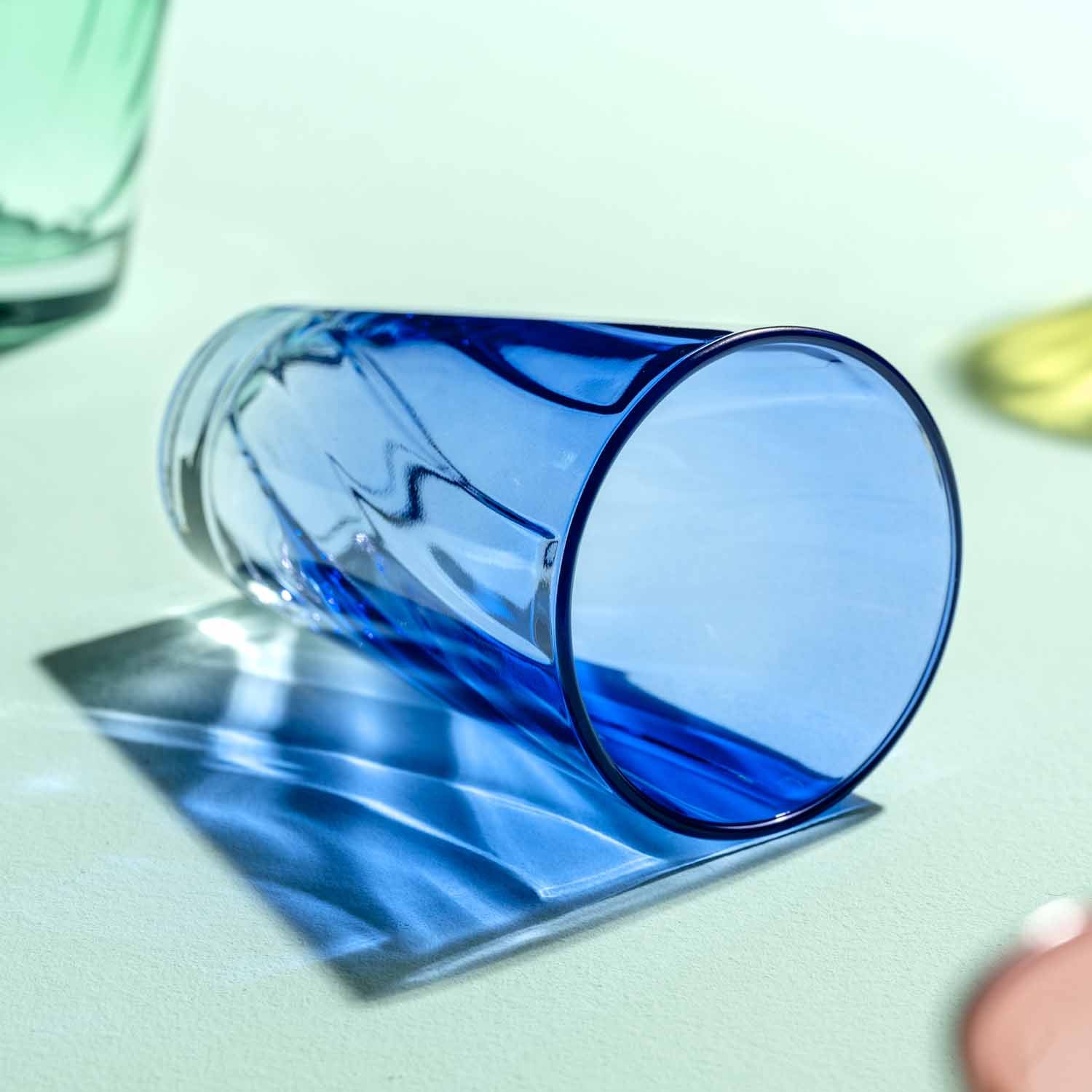 Blaues Trinkglas TWIST 300 ml auf heller Oberflaeche, leicht gekippt, mit Glasshadow