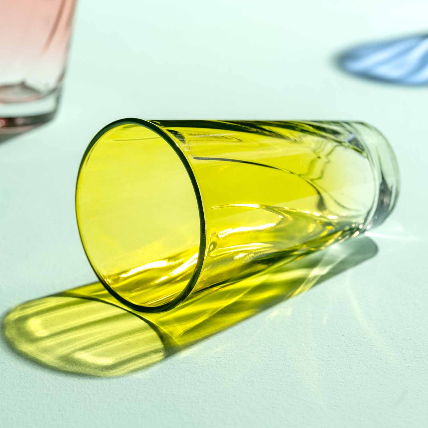 Gelbes Trinkglas TWIST 300 ml liegt auf weißer Oberfläche mit Schatten