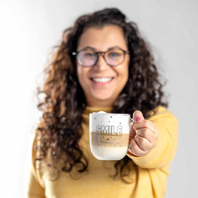 Frau mit Brille in gelbem Pullover hält Glastasse UFFICIO mit Gravur SMILE