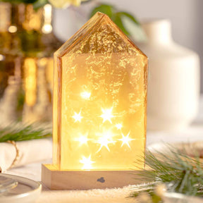 LED Haus 22 cm amber MAGICO mit leuchtenden Sternen, umgeben von Tannenzweigen auf Holzsockel