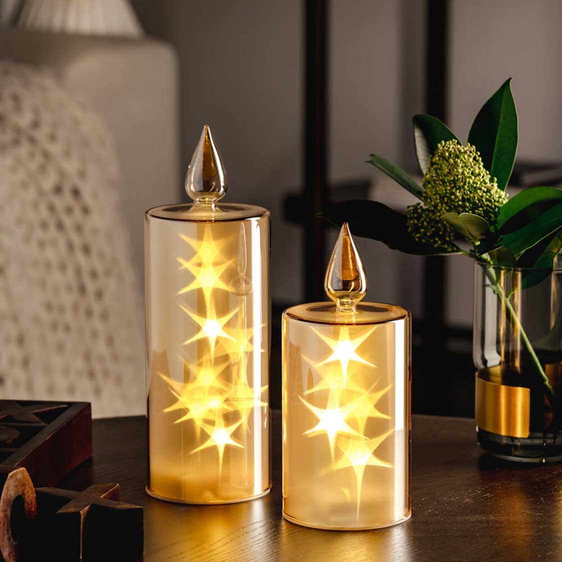LED Kerze CAPANNA gold mit Sternen auf Tisch neben Blumenvase