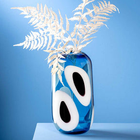 Vase OCCHI BLU mit weißen Augen-Motiven, gefüllt mit Wasser, Trockenblumen im Hals, blauer Hintergrund