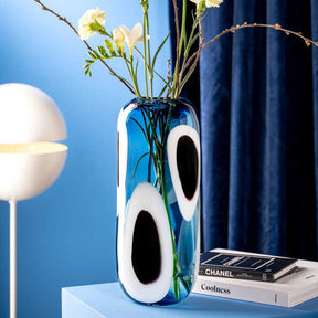 Vase OCCHI BLU mit weißen Augen-Motiven, gefüllt mit Blumen, auf blauem Tisch in Wohnraum