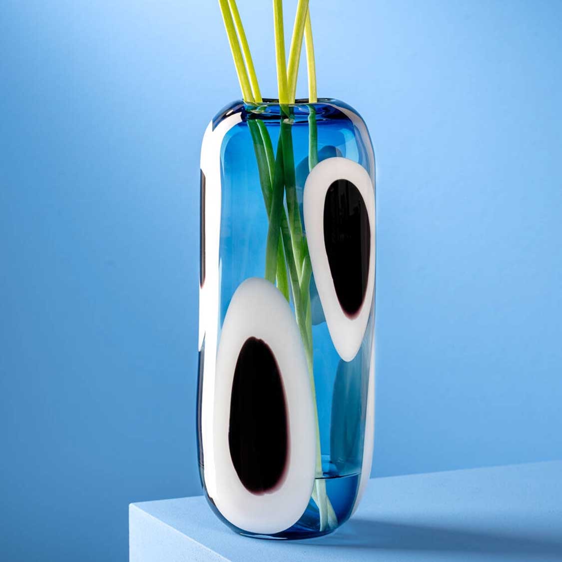 Vase OCCHI BLU mit weißen Augen und grünen Halmen vor blauem Hintergrund