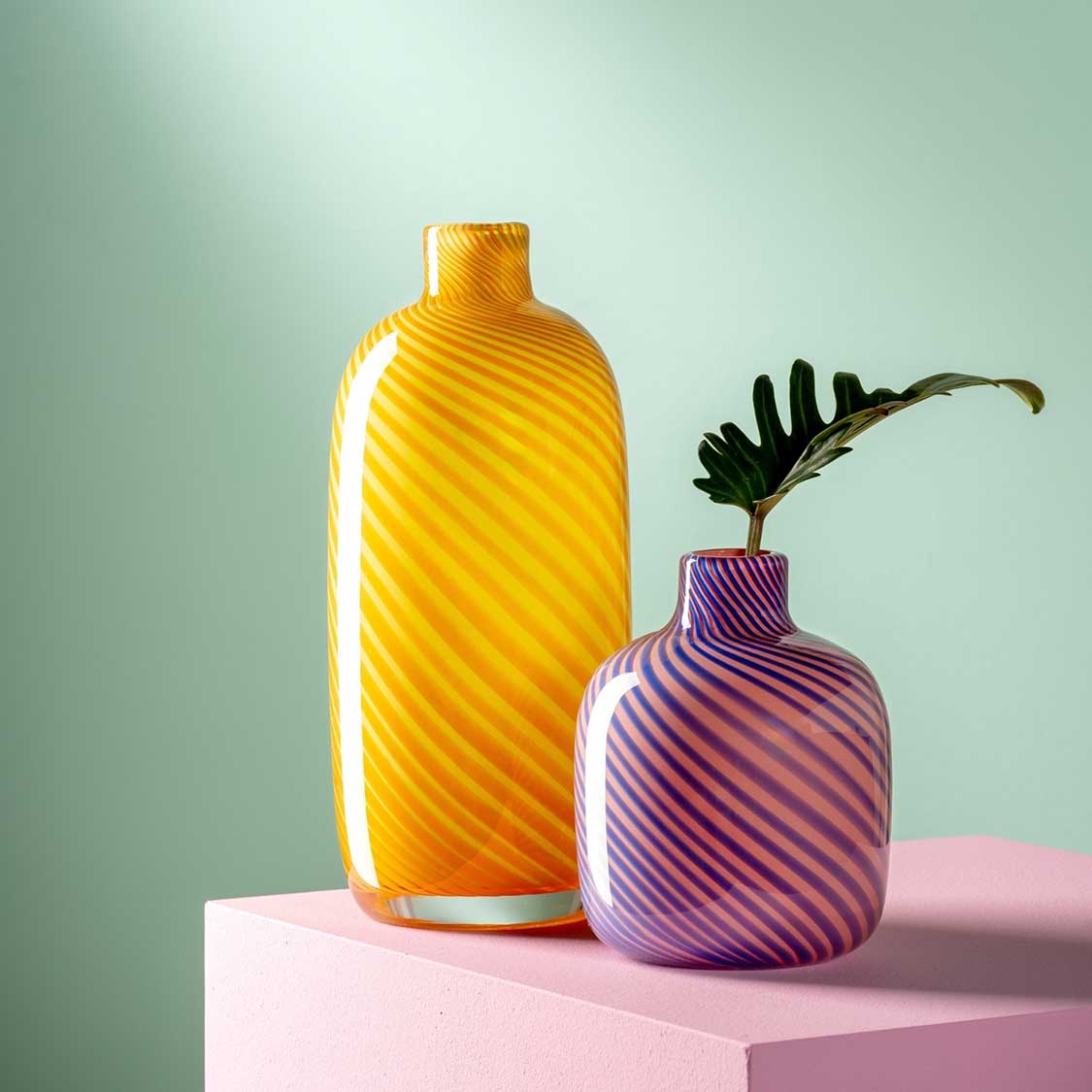 Vase FILO COLORI gelb neben lila Vase mit Pflanze auf rosa Podest