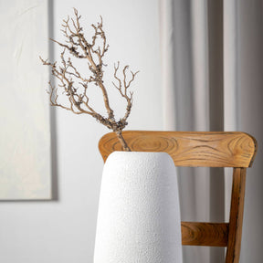 Zweig FIORE in weißer Vase auf Holzstuhl, helles Interieur