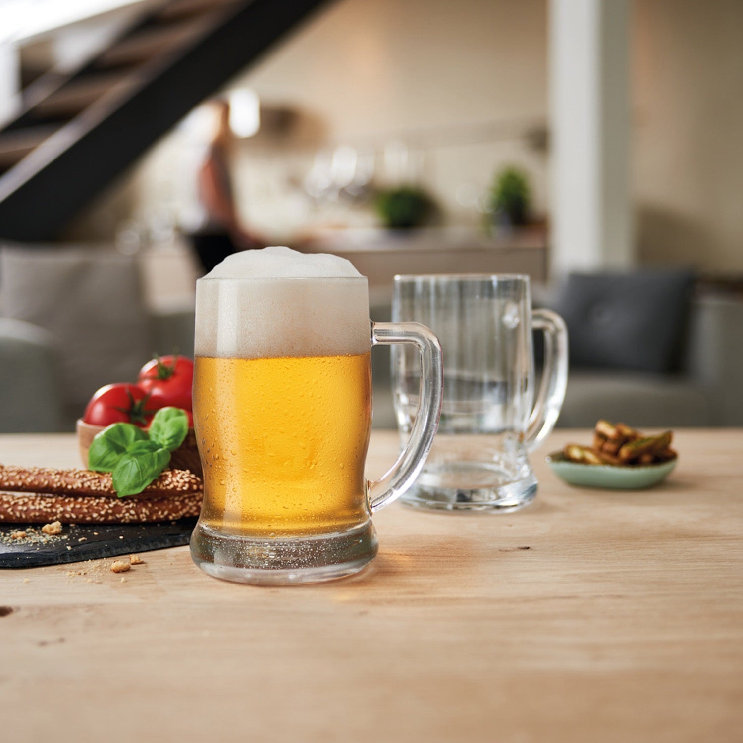 Gefüllter Bierseidel TAVERNA auf Holztisch in Wohnzimmer mit Snacks