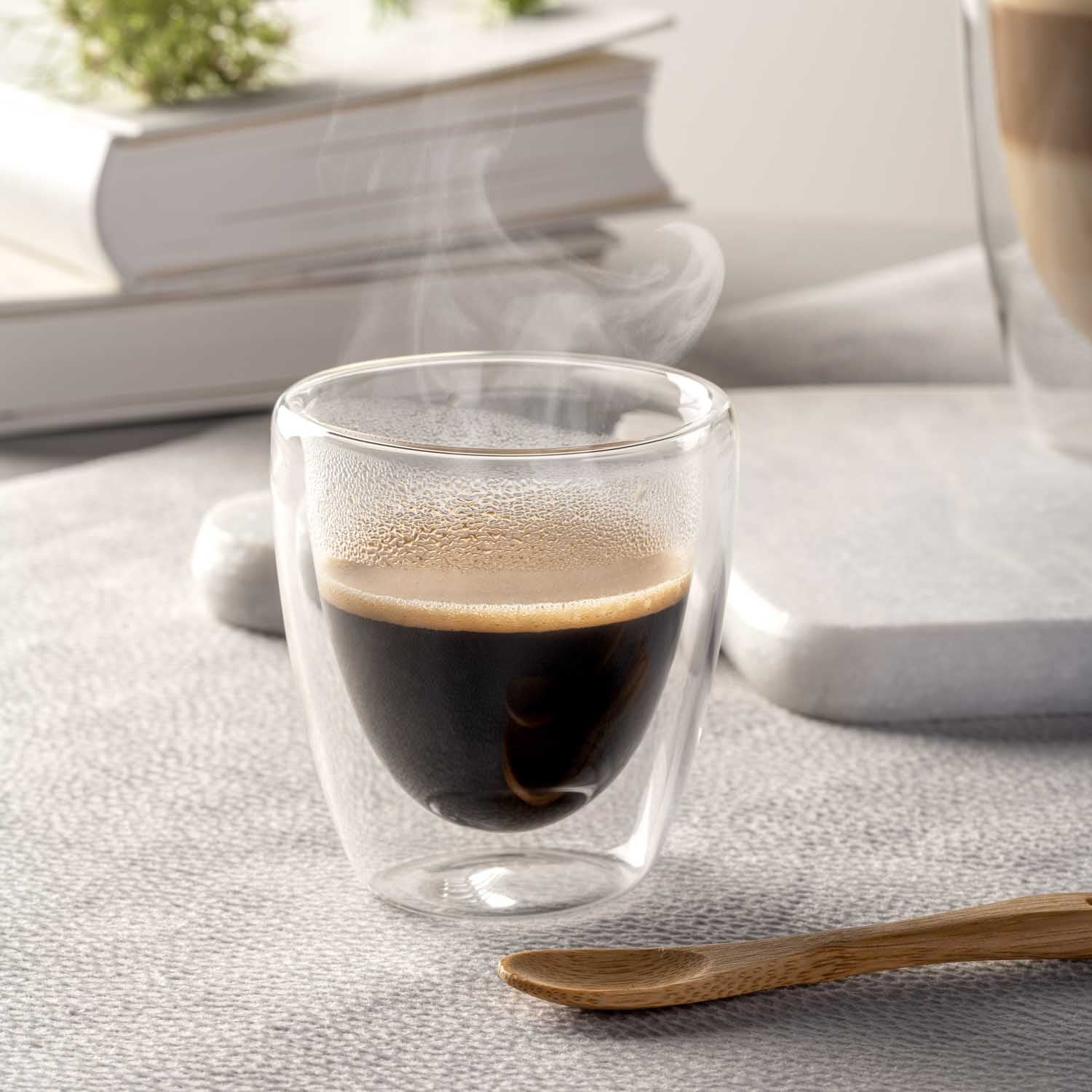 Doppelwandbecher Espresso DUO mit heißem Kaffee auf Schreibtisch, daneben Holzlöffel und Bücher