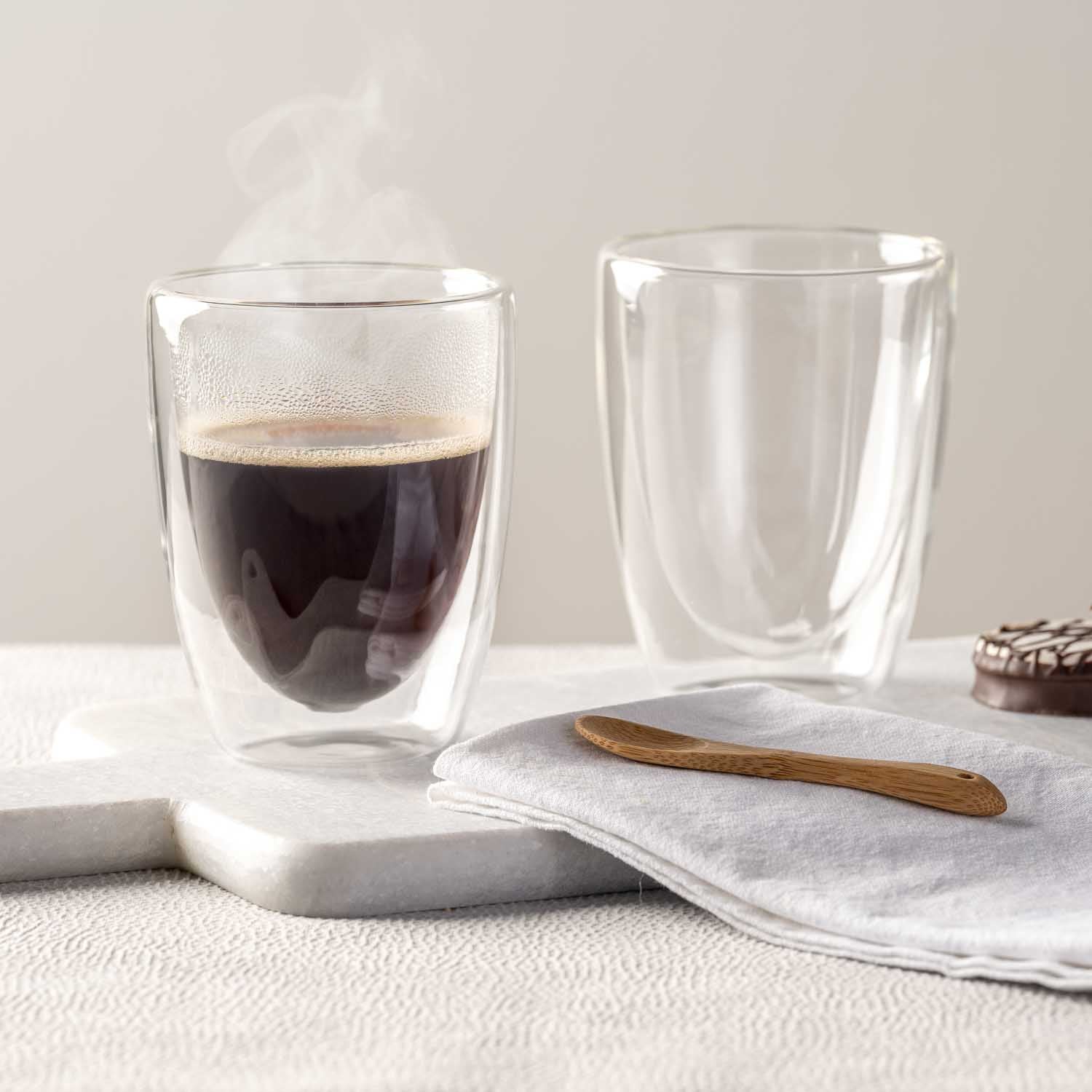 Doppelwandbecher DUO mit Kaffee und leerer Becher auf Untersetzer mit Leinentuch und Holzlöffel