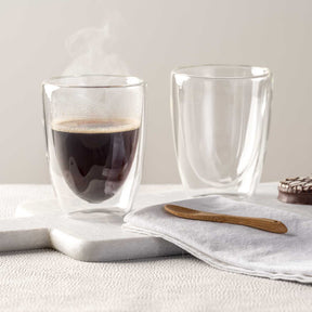 Doppelwandbecher DUO mit Kaffee und leerer Becher auf Untersetzer mit Leinentuch und Holzlöffel