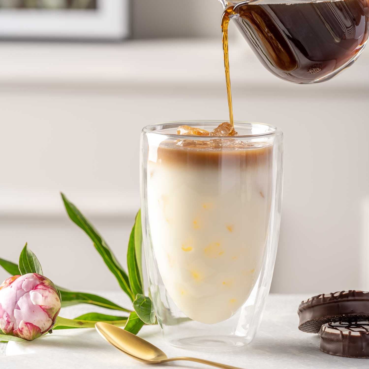 Doppelwandbecher DUO mit Kaffee, Milch und Blume auf Tisch