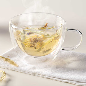 Teetasse DUO mit Kräutertee auf weißem Tuch, dampfend