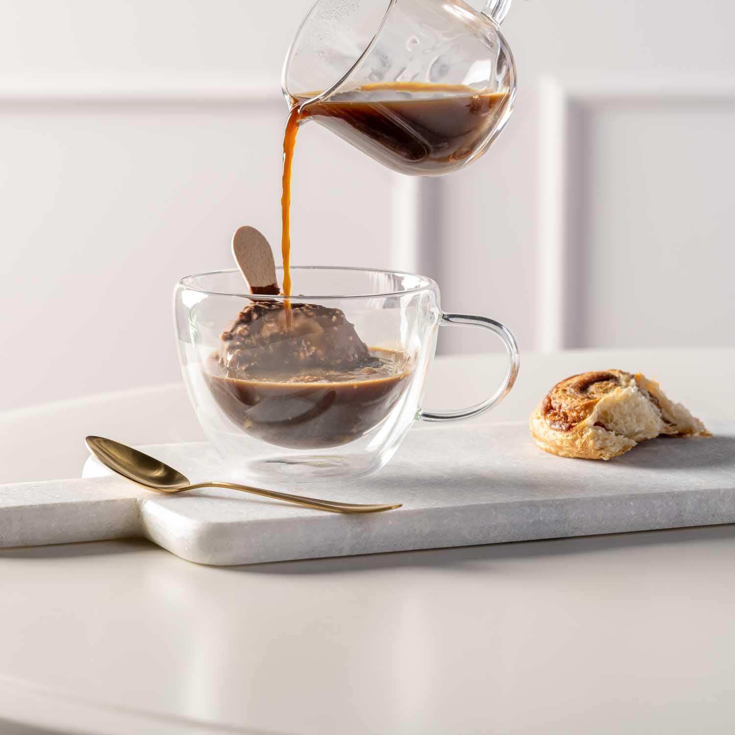 Teetasse DUO beim Eingießen von Kaffee, daneben Löffel und Gebäck auf Marmortablett