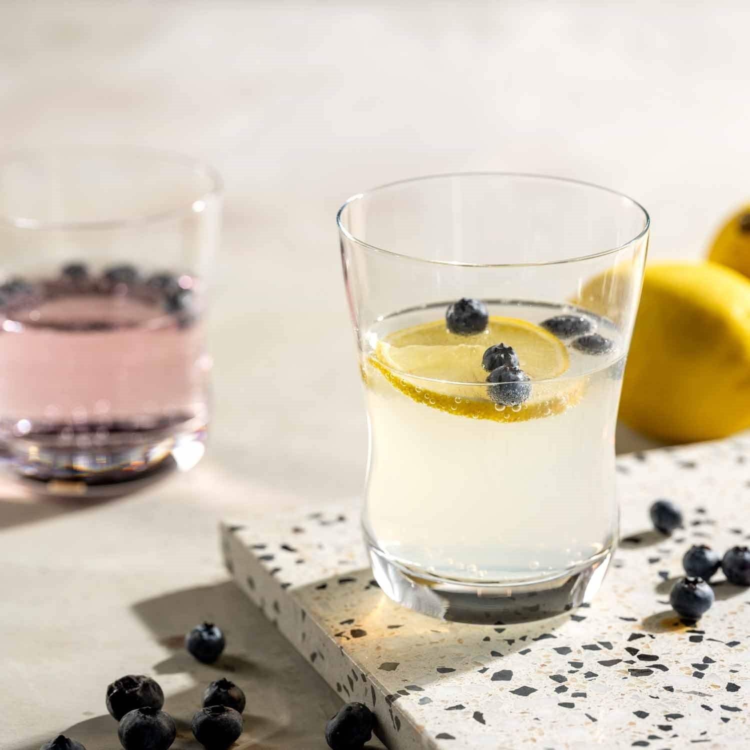 Trinkglas VITA mit Wasser, Zitronenscheibe und Heidelbeeren auf Terrazzo-Untergrund