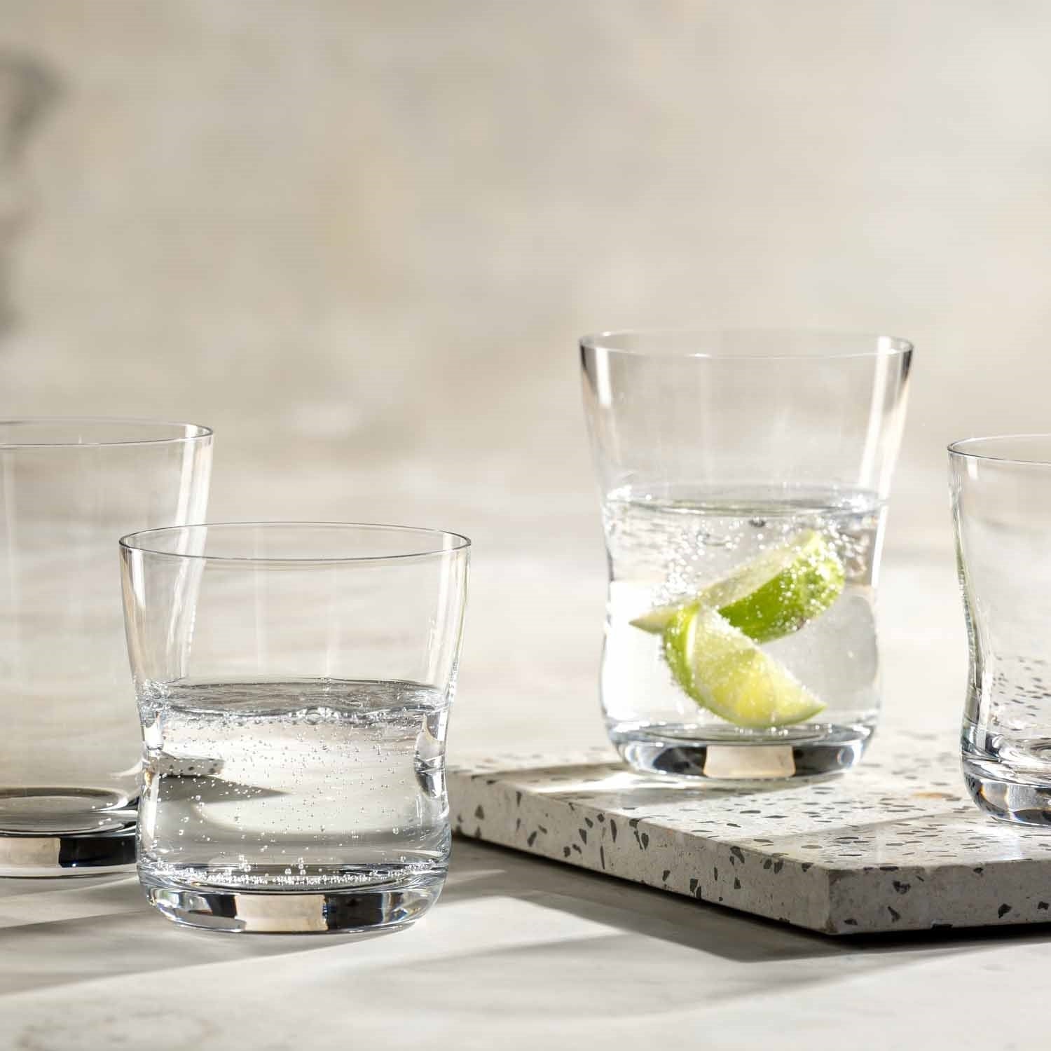 Trinkgläser VITA auf Betontablett, eines mit Limettenscheibe und Eiswürfeln