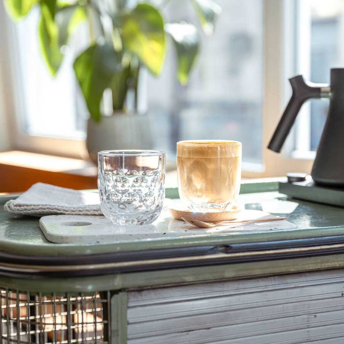 Espressoglas GOCCE 60ml 2er-Set auf Schreibtisch in Wohnraum, mit Wasser und Kaffee gefüllt