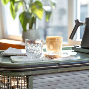 Espressoglas GOCCE 60ml 2er-Set auf Schreibtisch in Wohnraum, mit Wasser und Kaffee gefüllt
