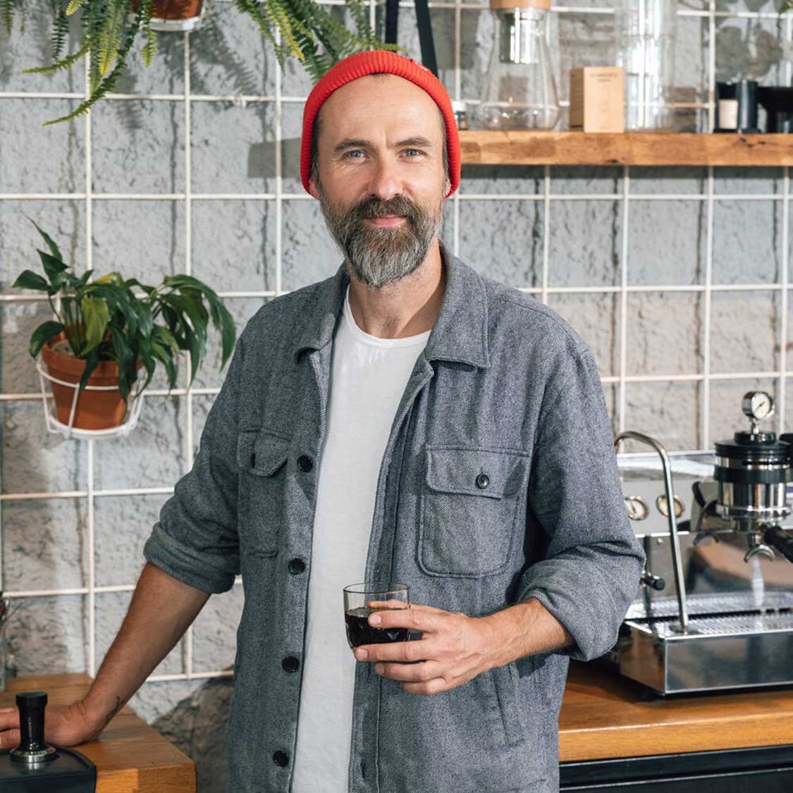 Mann mit rotem Beanie in Werkstatt hält Espressoglas GOCCE