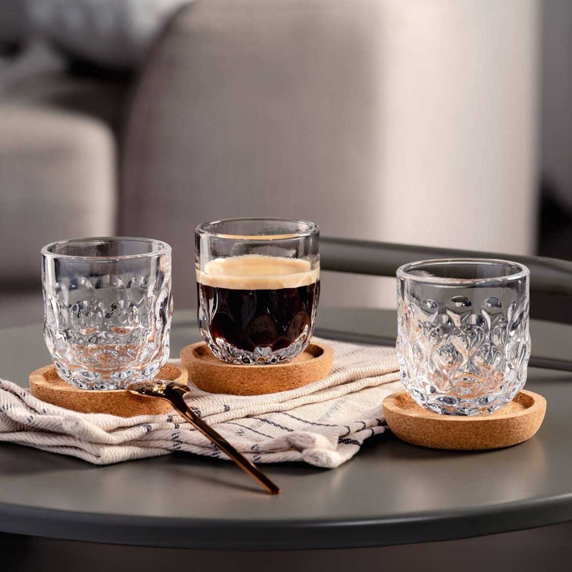 Espressoglas GOCCE auf Korkuntersetzern mit Getränken auf schwarzem Tisch