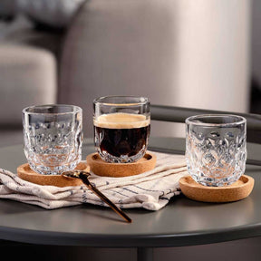 Espressoglas GOCCE auf Korkuntersetzer auf schwarzem Tisch mit Wasser und Kaffee