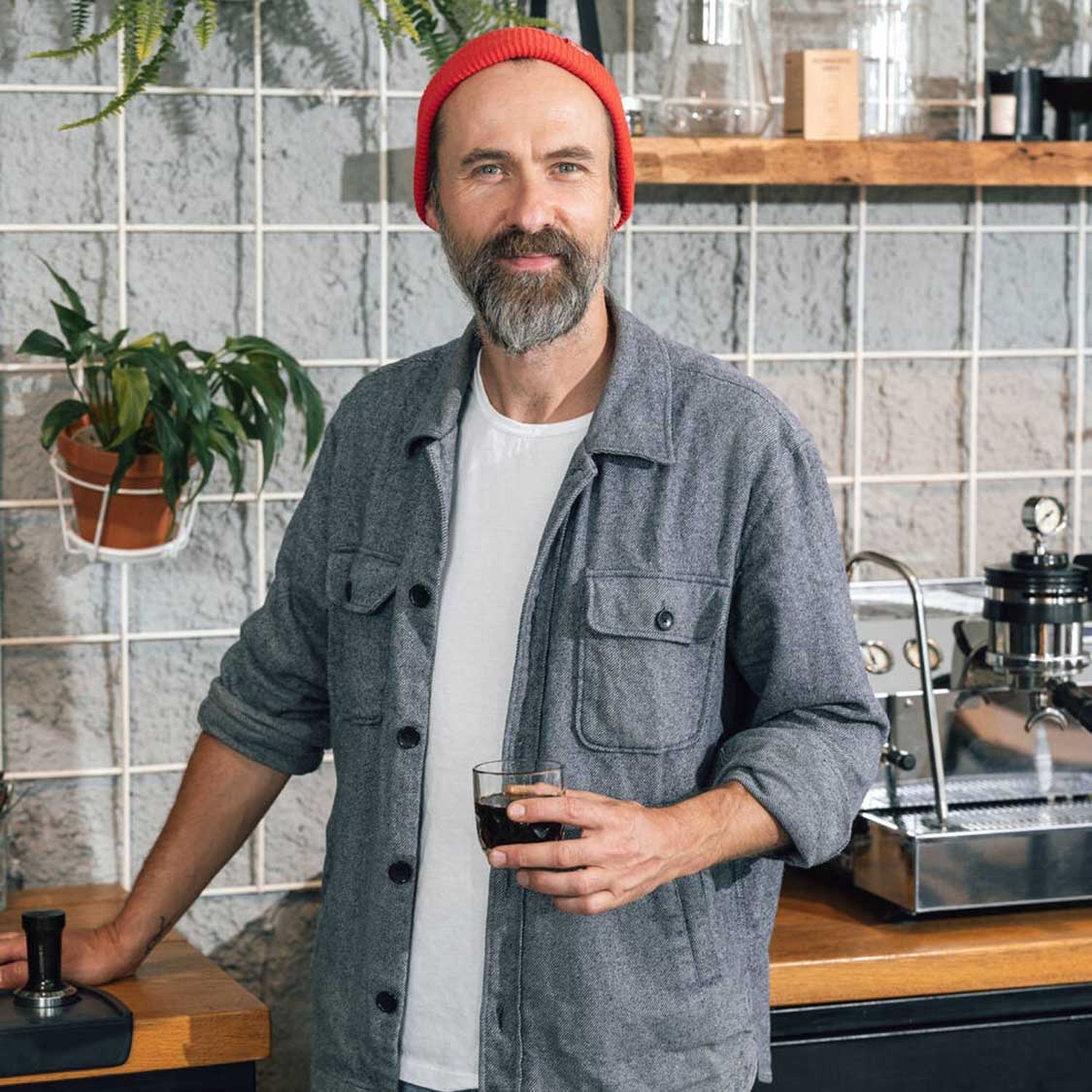 Mann mit rotem Wollmütze hält Espressoglas in Loft-Küche