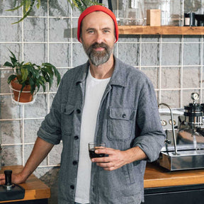 Mann mit rotem Wollmütze hält Espressoglas in Loft-Küche