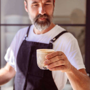 Mann in Schürze hält Kaffeeglas GOCCE 220ml mit Kaffee