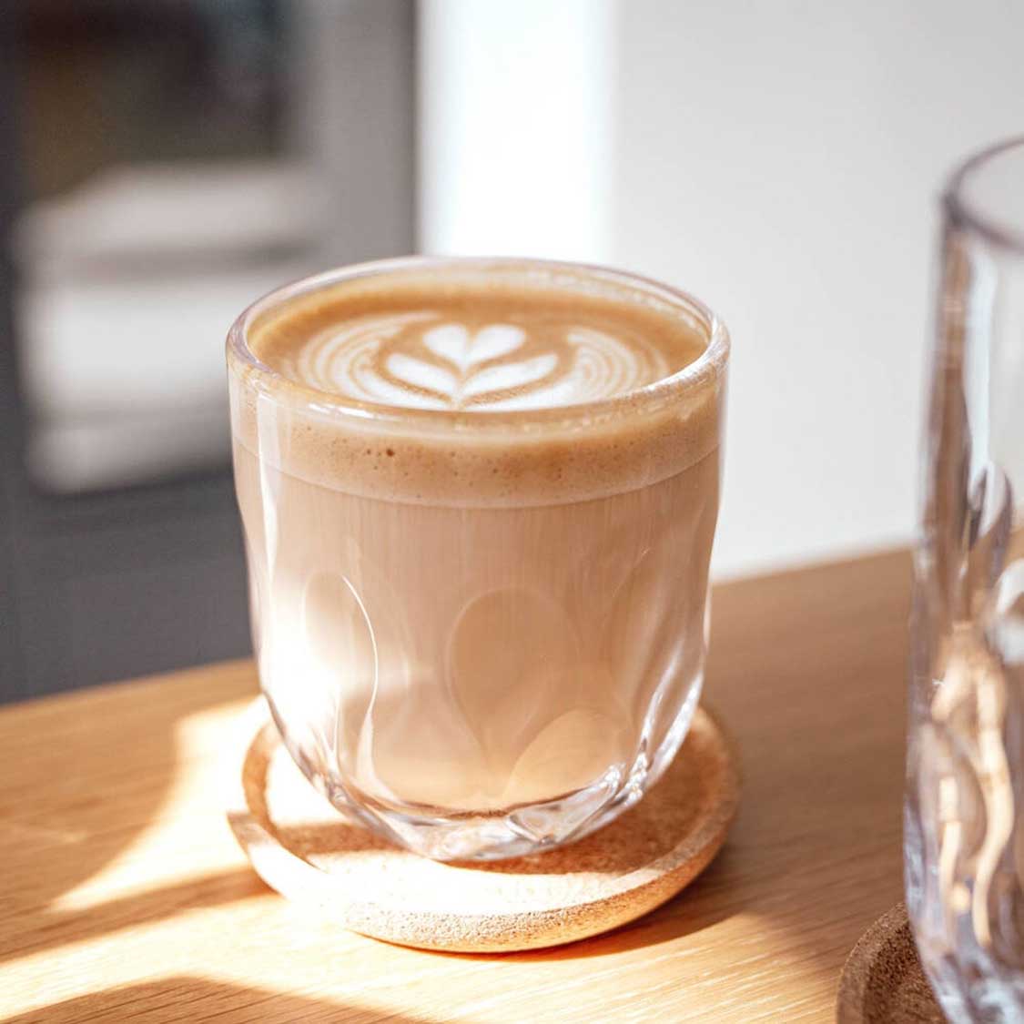 Kaffeeglas GOCCE mit Latte Art auf Holztisch in Tageslicht