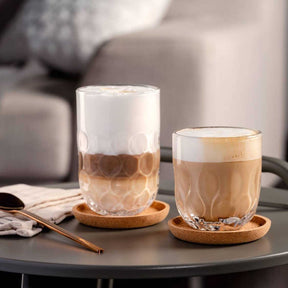 Zwei Latte Macchiato Gläser GOCCE mit Kaffeegetränk auf Korkuntersetzern im Wohnzimmer