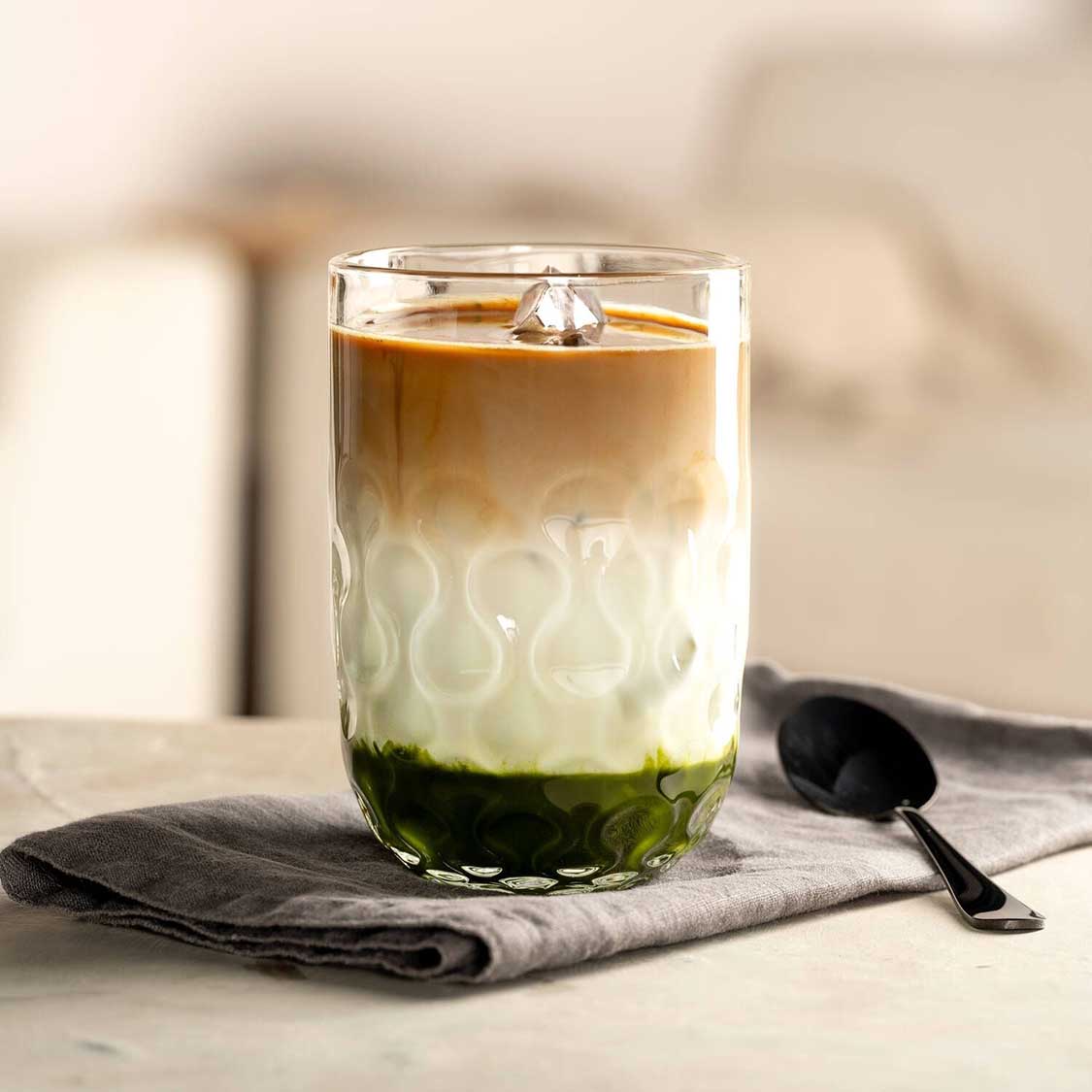 Latte Macchiato Glas GOCCE mit Iced Coffee auf Tuch, Loeffel daneben