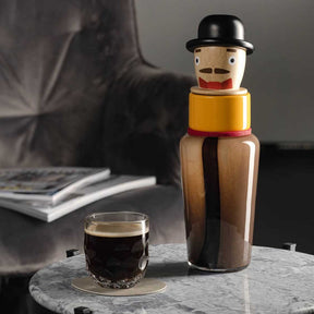 Untersetzer GOCCE braun auf Marmortisch, Glas mit Getränk, Holzfigur im Hintergrund