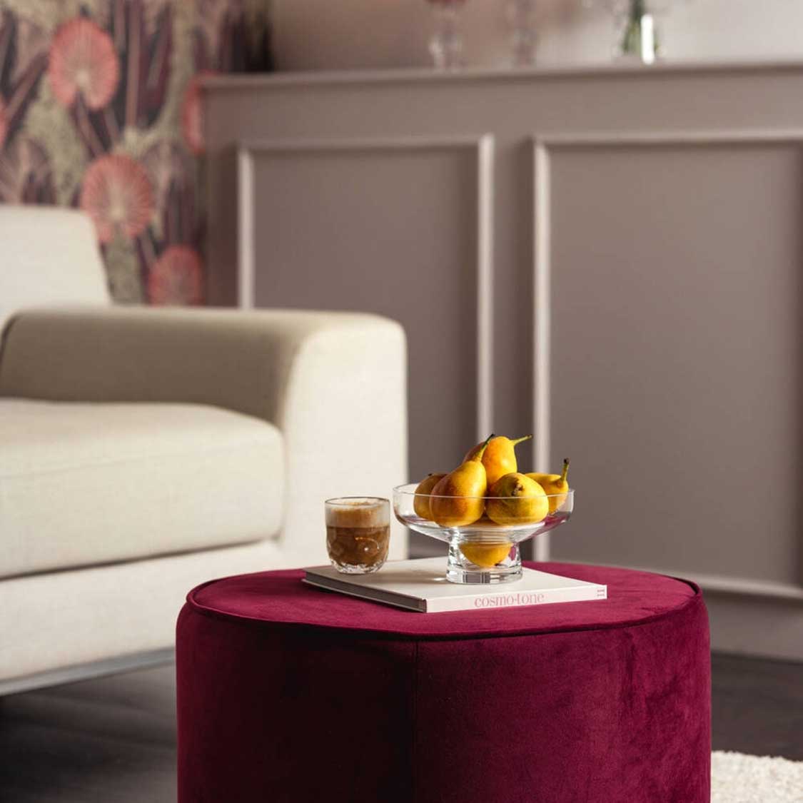 Glasvase auf burgunderfarbenem Pouf in Wohnzimmer mit Obst und Getränk