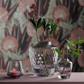 Drei Glastischlichter mit Blumen in Vase auf Tisch