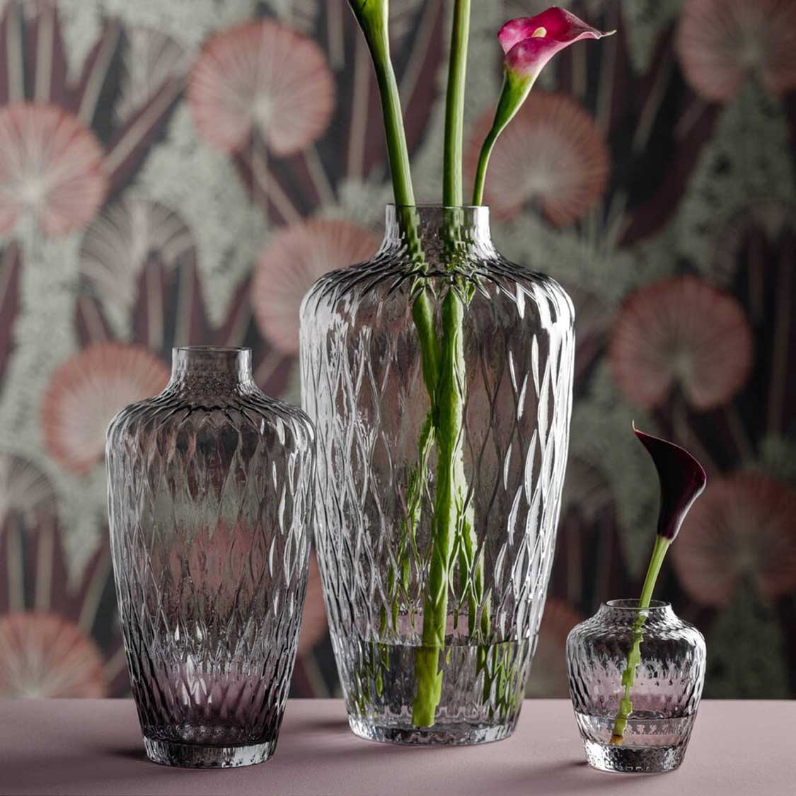 Drei graue Glasvasen der Serie GIULIA mit Blumen vor gemustertem Hintergrund