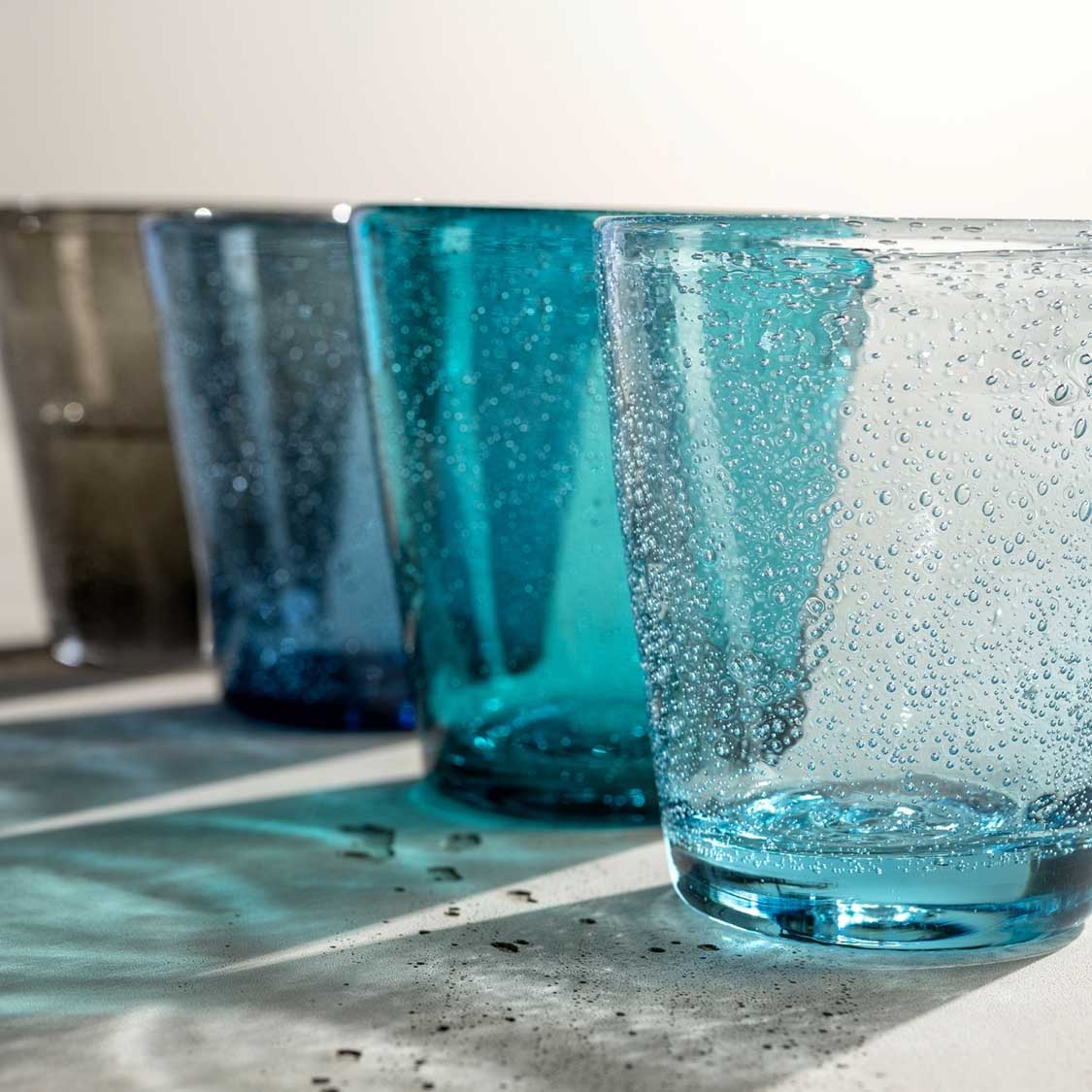 Vier Trinkgläser BURANO in Blau- und Türkistönen mit Wasser und Blasen gefüllt