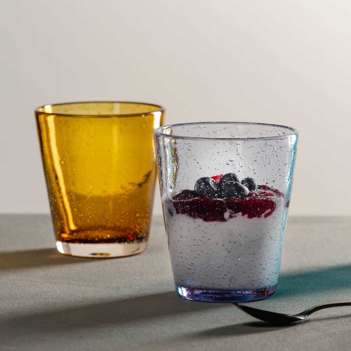Zwei Trinkgläser mit Getränken, links gelb, rechts transparent mit Beeren