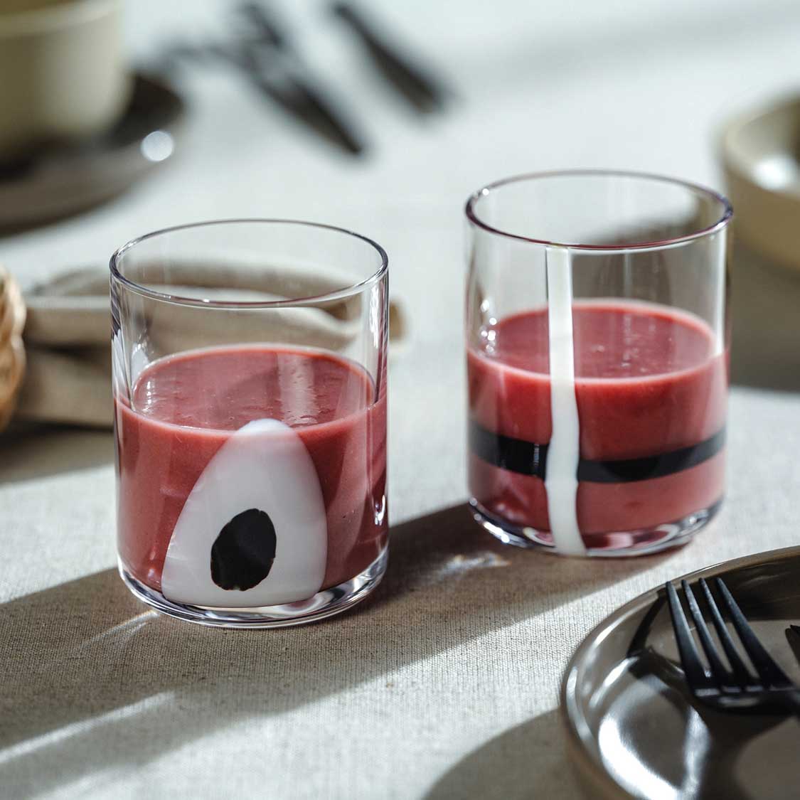 Zwei Trinkgläser BANDA NERA mit roter Flüssigkeit auf gedecktem Tisch, schwarze Streifen sichtbar