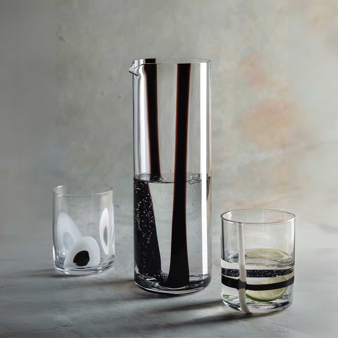 Drei Gläser mit schwarzen Streifen: Wasserglas, hohe Kanne mit Wasser und Glas mit grünem Getränk
