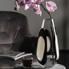 Vase OCCHI BIANCHI mit Orchideenzweig auf Marmortisch, neben Glas und Stuhl