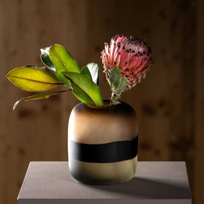 Vase CORSO SABBIA mit grünen Blättern und rosa Protea auf grauem Untergrund