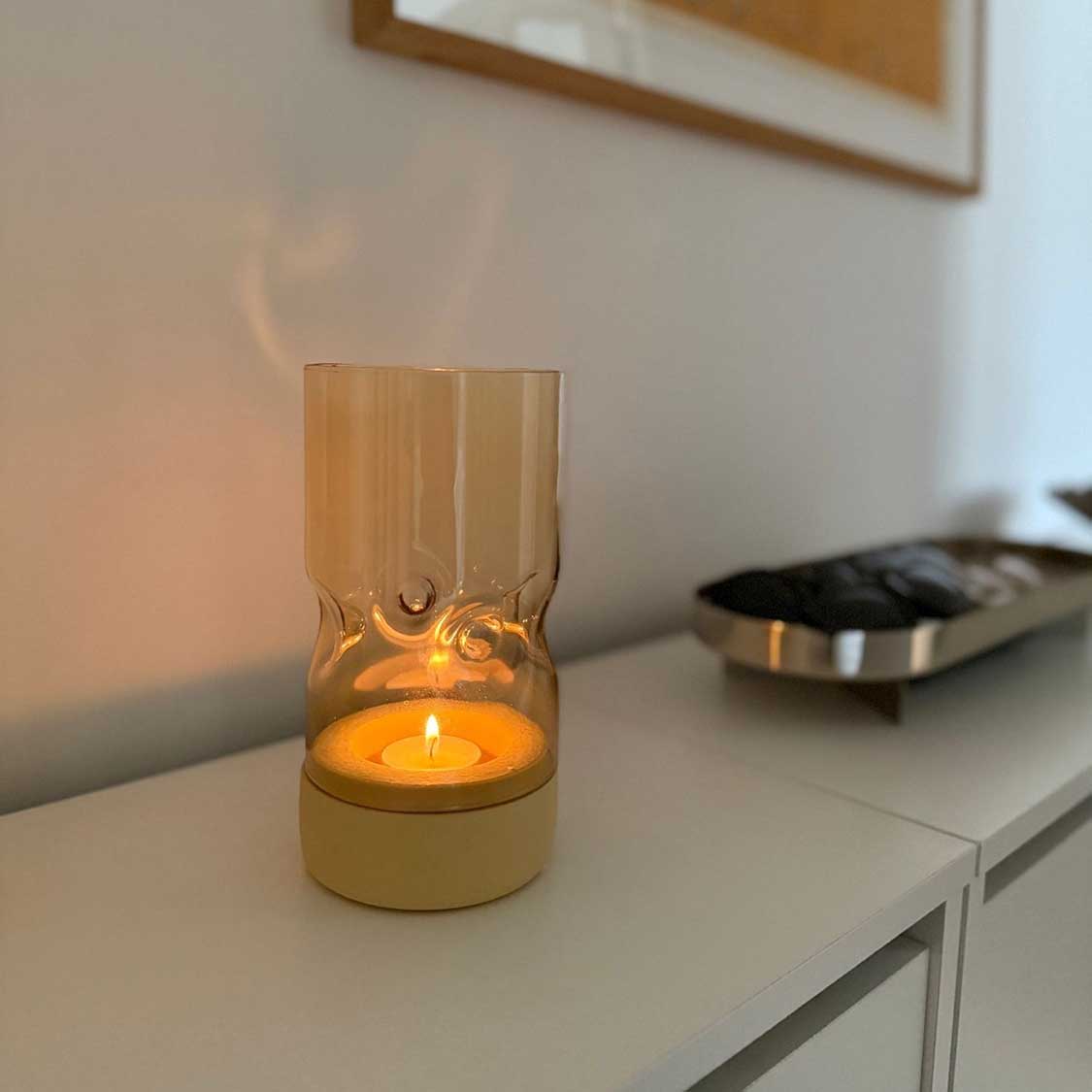 Tischlicht auf Sockel SOLE auf weißem Sideboard in Wohnraum, brennende Kerze sichtbar