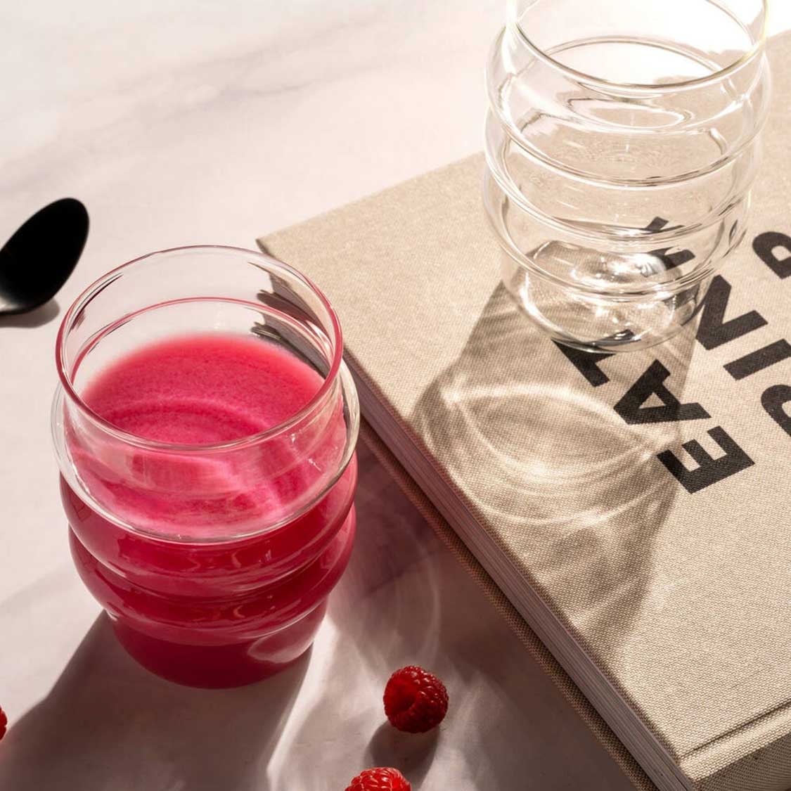 Trinkglas SOLE 440 ml mit Getränk und Wasser, daneben Zeitschrift und Beeren