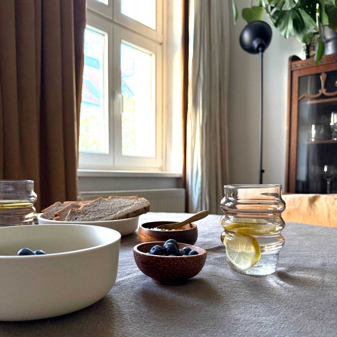 Trinkglas SOLE auf gedecktem Tisch mit Wasser, Obst und Brot