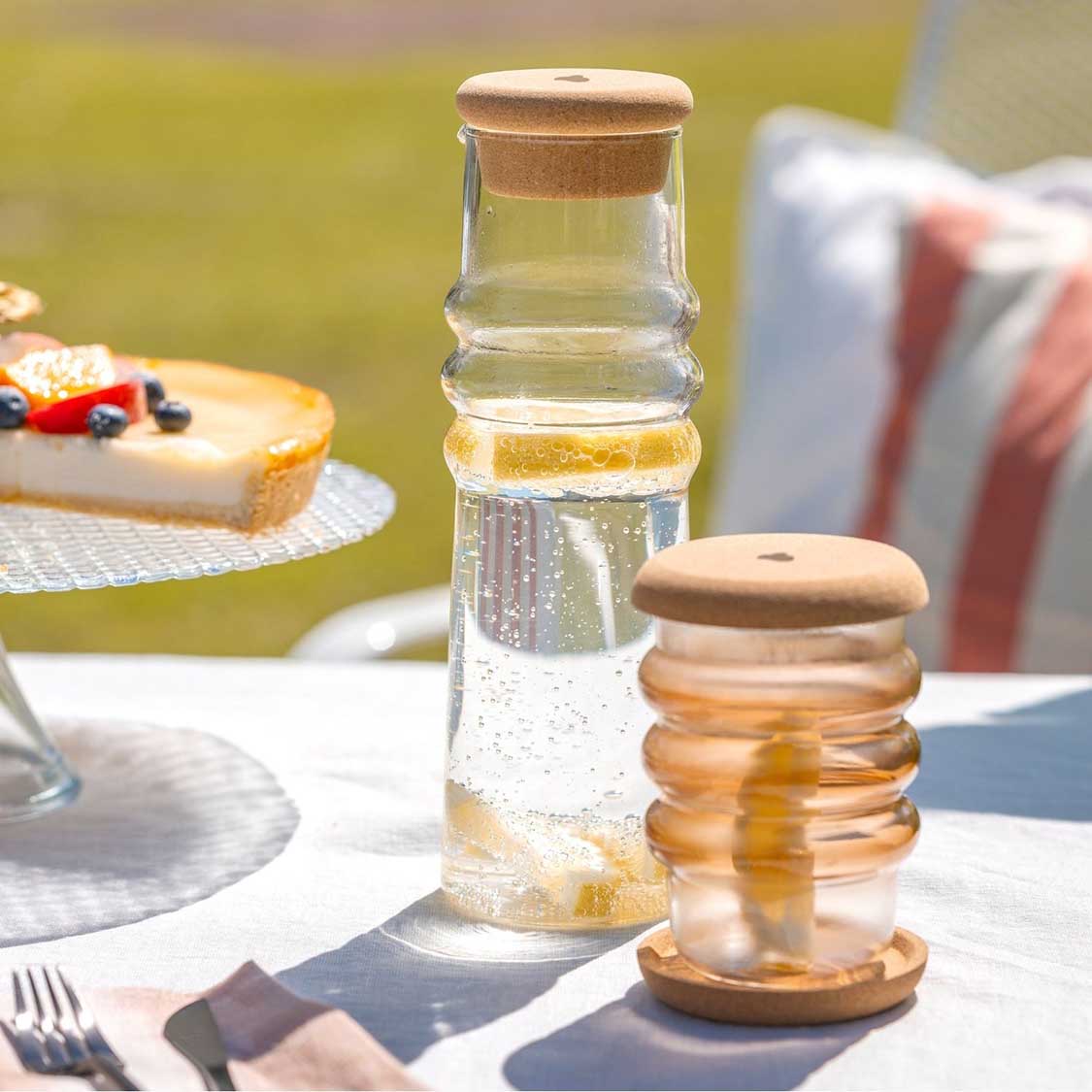 Karaffe SOLE mit Wasser auf gedecktem Tisch, daneben Gläser und Torte