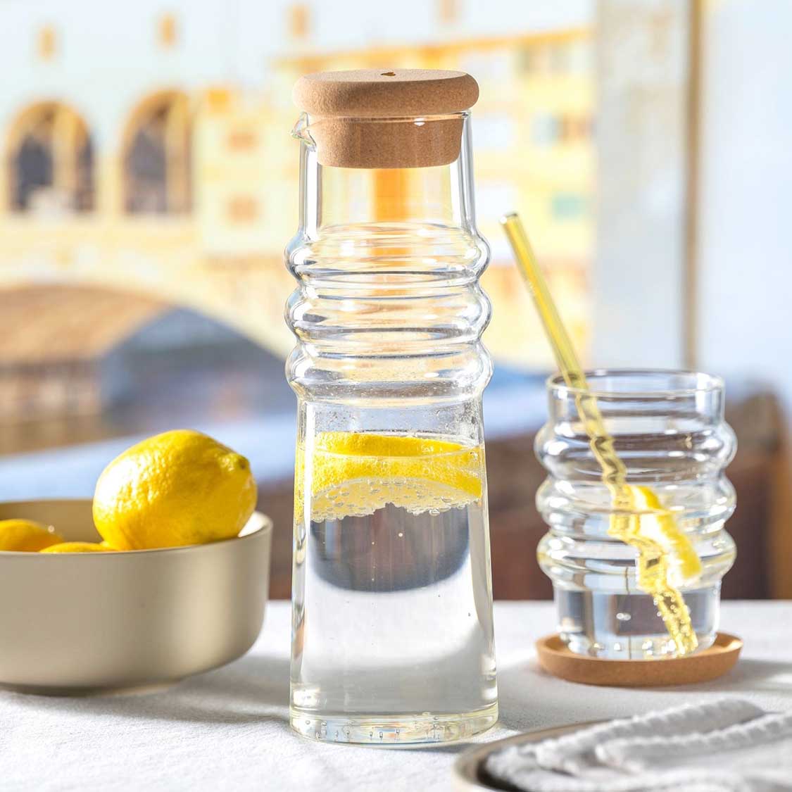 Karaffe SOLE mit Korkstopfen auf gedecktem Tisch, Zitrone und Glas mit Strohhalm