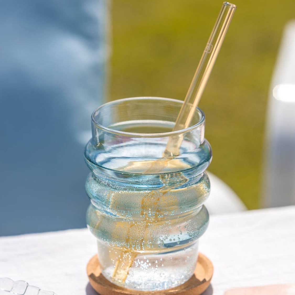 Glastrinkhalm in Glas mit Wasser und Eis, Holzuntersetzer, unscharfer Hintergrund