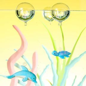 Blaue Glaskugeln mit Delfinen und farbigen Grashalmen in gelber Umgebung