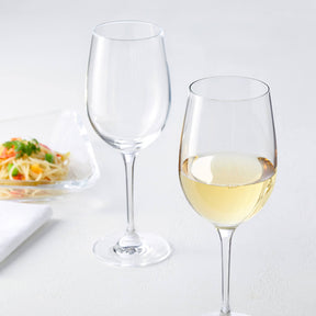 Weißweinglas CIAO+ mit Wein gefüllt neben leerem Glas, Teller mit Pasta im Hintergrund
