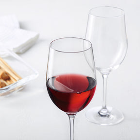 Rotweinglas CIAO+ mit Rotwein gefüllt, daneben leeres Glas, auf weißem Tisch mit Serviette und Appetizer
