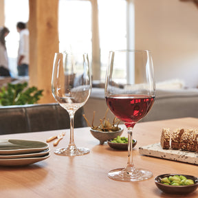 Rotweinglas CIAO+ mit Rotwein auf gedecktem Tisch, Gäste im Hintergrund
